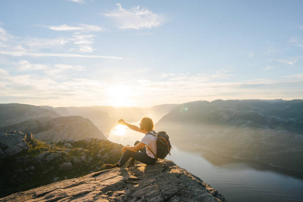 Young Caucasian man sitting on Preikestolen and making selfie  at sunrise